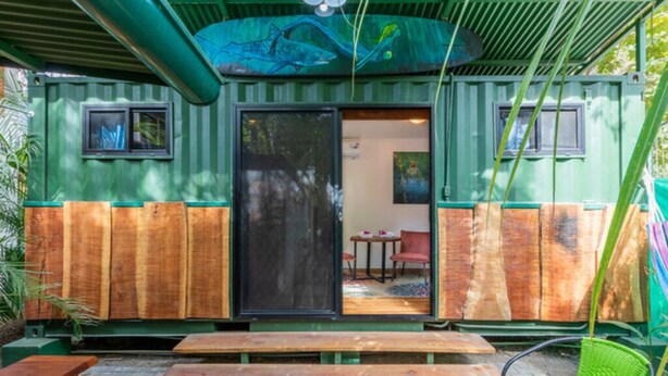 A green container-style building with a sliding door, wooden benches, and a green chair outside. - The Surf Shack - With direct beach access (Playa Guiones)