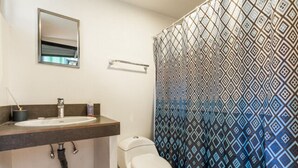 A bathroom with a white sink, mirror, toilet, and patterned shower curtain. - The Surf Shack - With direct beach access (Playa Guiones)