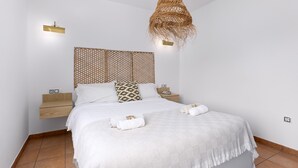 A neatly made bed with white linens, a woven headboard, bedside tables with lamps, and a hanging rattan light fixture. - Home2Book Casa Calma Garden, Pool & Relax (Majanicho)