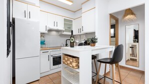 A modern kitchen with white cabinetry, a central island, a refrigerator, an oven, and a dining area with a chair and table. - Home2Book Casa Calma Garden, Pool & Relax (Majanicho)