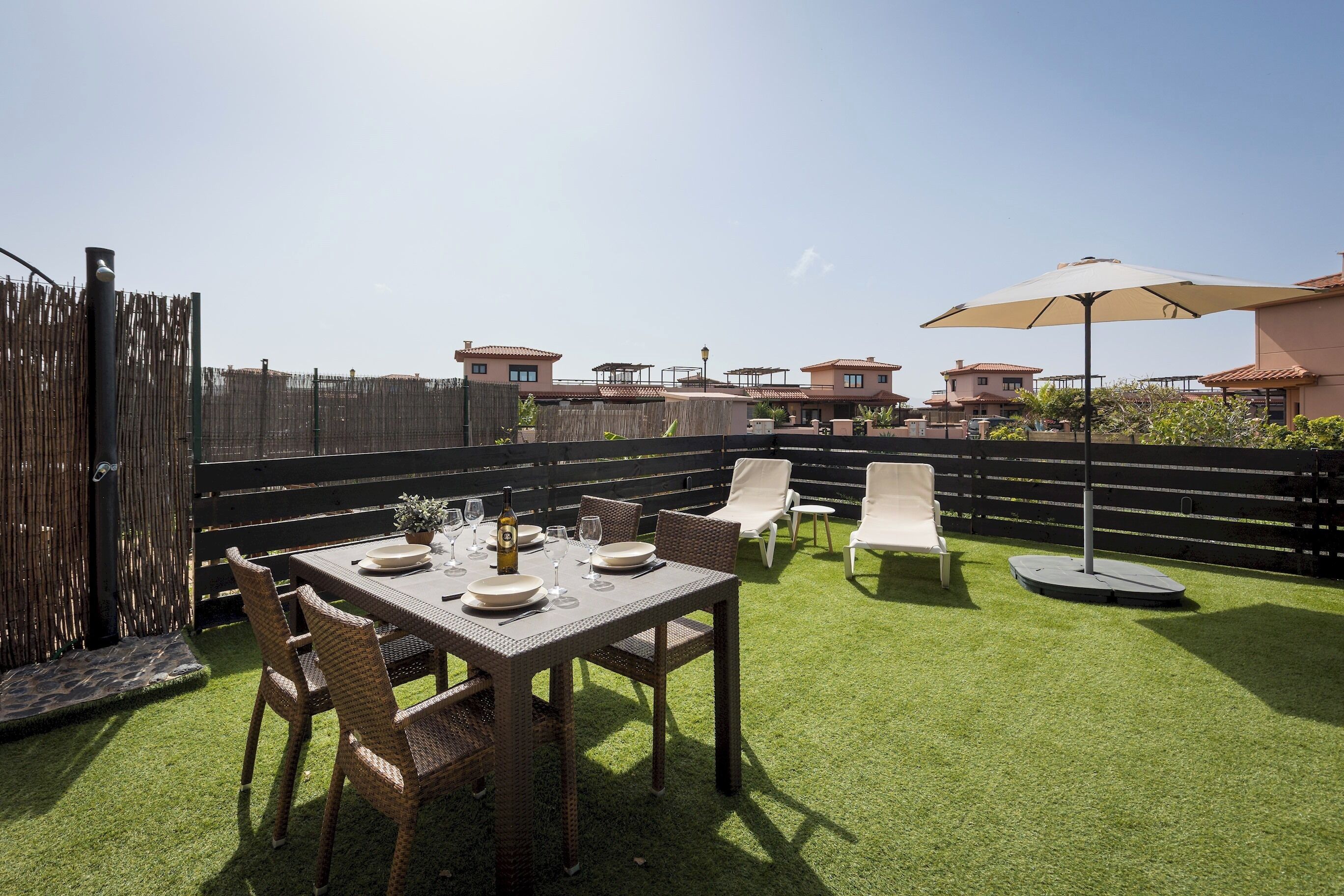 Une terrasse avec une table dressée pour le repas, des chaises d’extérieur et un parasol.