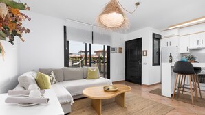 A modern living room with a sofa, coffee table, and kitchen area with cabinets and a bar stool. - Home2Book Casa Calma Garden, Pool & Relax (Majanicho)