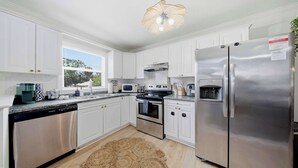 A modern kitchen with white cabinets, stainless steel appliances, a large refrigerator, and a ceiling fan.