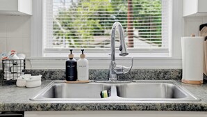 A kitchen with a stainless steel sink, a window with blinds, and soap dispensers on the counter.