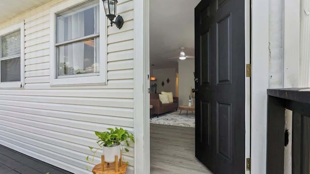 A wooden deck with a potted plant, a black door, and a living room with a couch and a rug.