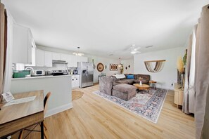 A modern kitchen with white cabinets, a dining table with chairs, a sofa, and a decorative rug.