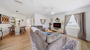 A living room with a sofa, a dining area with a table and chairs, a television, and a ceiling fan.