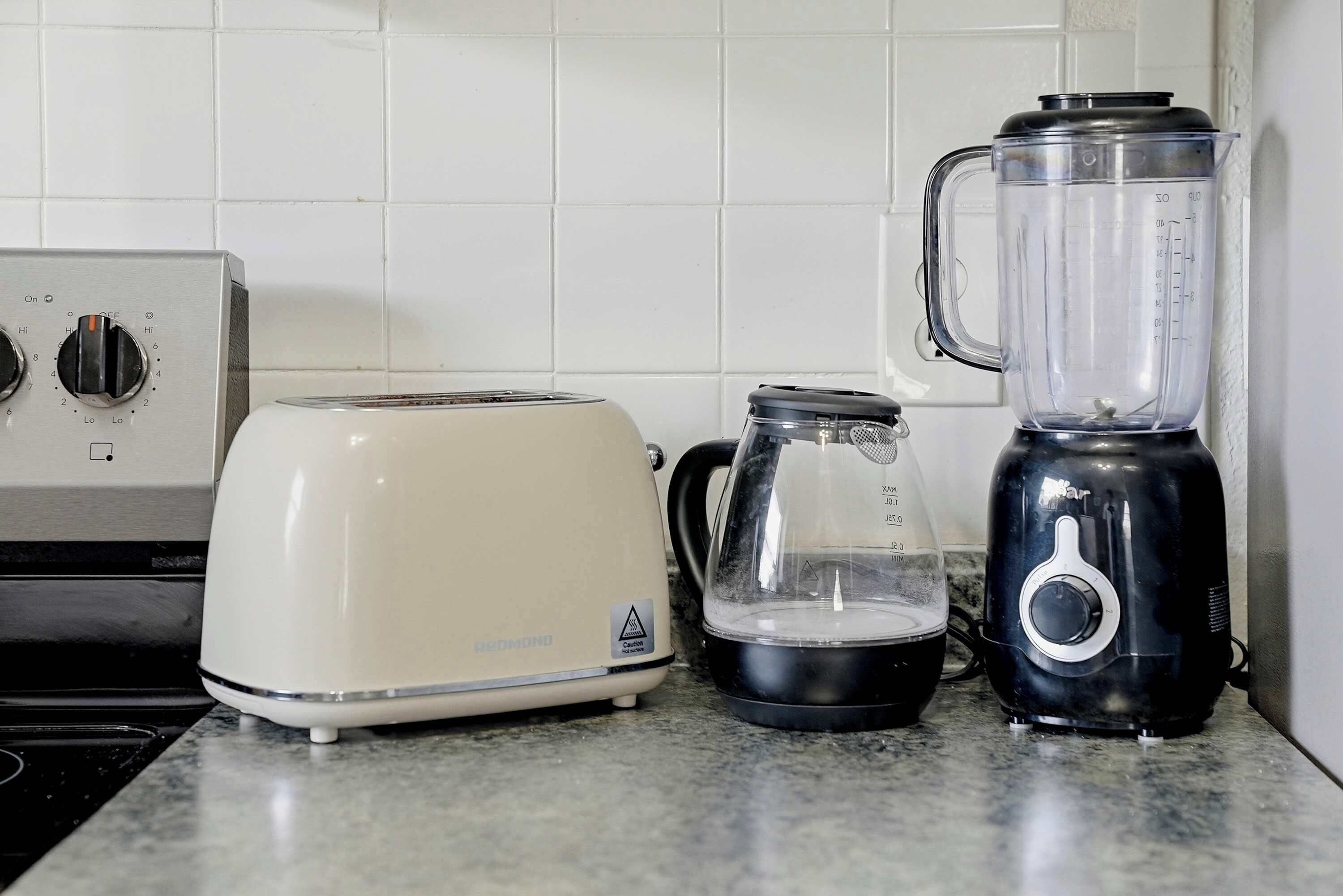 A kitchen with a white toaster, a black blender, and a clear glass pitcher on a granite countertop.