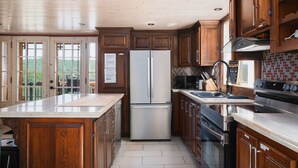 A modern kitchen with wooden cabinets, a stainless steel refrigerator, a built-in oven, and a large island with a sink. - Charming log cabin nestled in the woods, with a spa and in-ground pool.  (Mandeville)