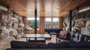 A cozy indoor space with a stone wall, wooden ceiling, and a pool table. - Charming log cabin nestled in the woods, with a spa and in-ground pool.  (Mandeville)