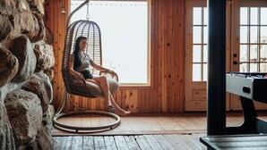 A wooden cabin interior with a stone wall, a hanging chair, and a pool table. - Charming log cabin nestled in the woods, with a spa and in-ground pool.  (Mandeville)