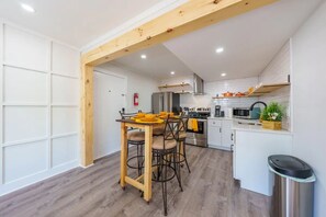 Een moderne keuken met witte kastjes, roestvrijstalen apparatuur en een houten eettafel met stoelen.