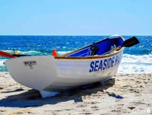 Een klein bootje met de tekst 'SEASIDE PARK' op de zijkant, geparkeerd op een zandstrand met de oceaan op de achtergrond.