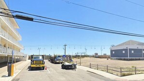 A parking area with a yellow truck, a blue building, and a fenced area with a ski lift in the background. - Modern Seaside Condo, 2 Blocks to Sand+ Parking - a Seaside Heights Sanctuary! (Seaside Heights)