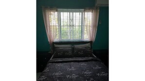 Een slaapkamer met een bed belegd met een donkere hoeslaken met daarop 'Je t'aime' gedrukt, een raam met transparante gordijnen en teal muren.