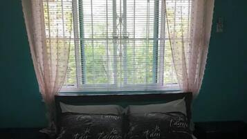 A bedroom with a bed covered in a dark sheet with 'Je t'aime' printed on it, a window with sheer curtains, and teal walls.