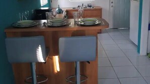Een keuken met een centraal eiland, twee barkrukken, houten keukenkastjes, een raam en een koelkast.