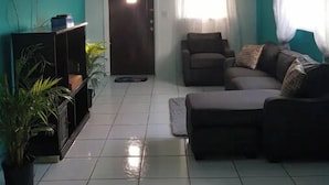 Een woonkamer met een plafondventilator, een aan de muur bevestigde televisie, een bank en een salontafel.