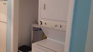 Un lavadero pequeño con lavadora y secadora blancas, un bote de basura y una pared azul.