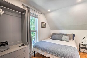 Ein Schlafzimmer mit einem Bett, einem Nachttisch, einem Fenster mit Vorhängen und einem an der Wand befestigten Regal.