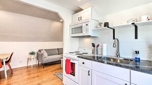 Une cuisine compacte avec des appareils électroménagers blancs, un canapé gris et un coin repas comprenant une table et des chaises en bois.