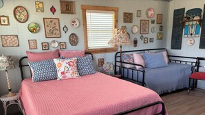 A bedroom with two beds, a wooden floor, and a wall decorated with various framed pictures and plates.