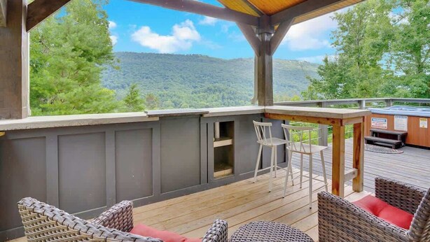 Terraza exterior con mobiliario de mimbre, techo de madera y vista a una ladera boscosa.
