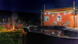 Un bain à remous avec des sièges, un foyer et un bâtiment en bois décoré de guirlandes lumineuses.