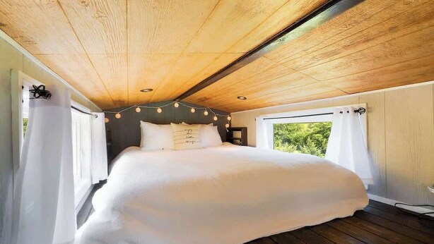 Une chambre avec un plafond en bois, un grand lit et une vue sur la verdure par la fenêtre.