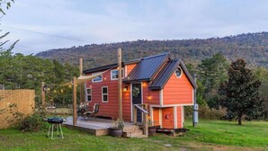 Une maison rouge avec une terrasse, entourée d’une cour verdoyante et d’arbres.