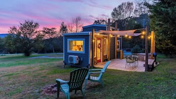 Une petite maison dotée d’une terrasse, d’un espace salon extérieur et d’un porche illuminé de guirlandes lumineuses.