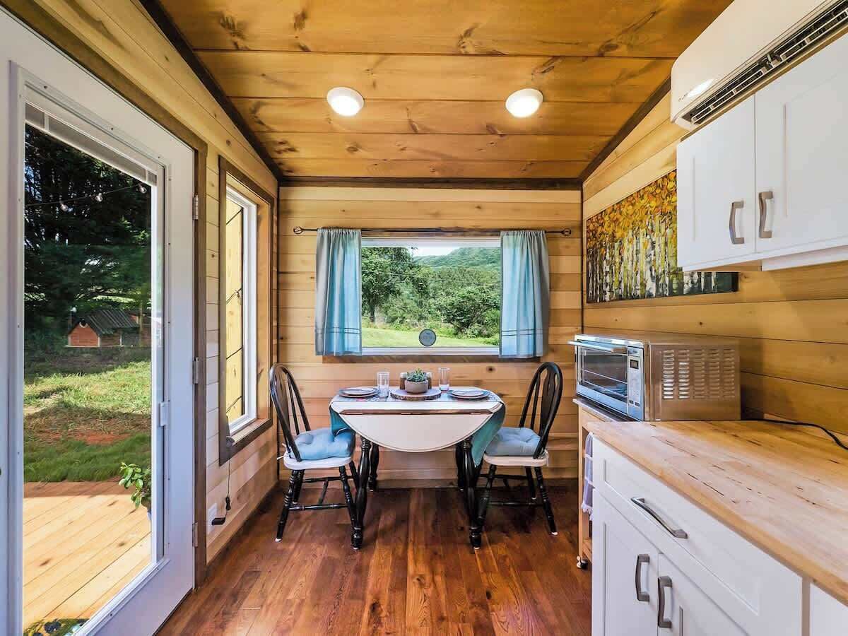 Un intérieur en bois comprenant une table à manger, des chaises, un four à micro-ondes et une vue sur la verdure à l’extérieur.