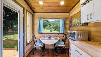 Un intérieur en bois comprenant une table à manger, des chaises, un four à micro-ondes et une vue sur la verdure à l’extérieur.