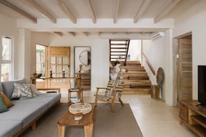 A spacious living area with a sofa, wooden furniture, a staircase, and a TV.