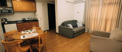 A compact living space with a dining area, kitchenette, grey sofa, and a small armchair.
