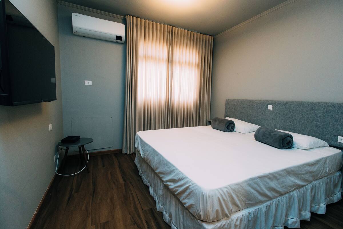 A hotel room with two beds, an air conditioning unit, a small table, and a TV mounted on the wall.