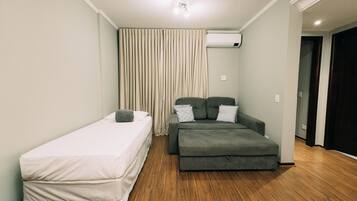 A room with a single bed, a sofa, and a wooden floor.