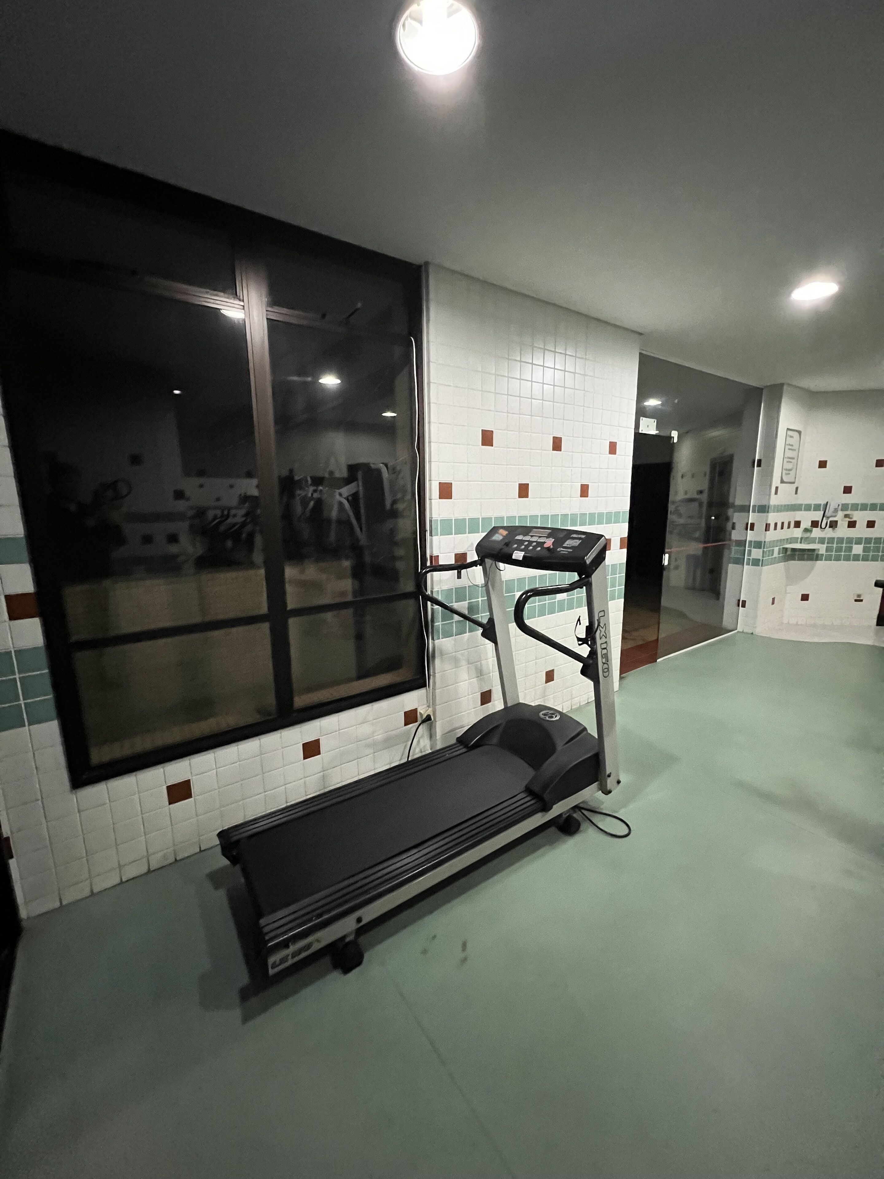 Un gimnasio con cinta de correr, pared con espejos y suelo de baldosas.