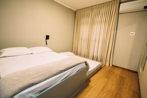 Ett hotellrum med en säng, en telefon som sitter fast på väggen och ett fönster med gardiner.