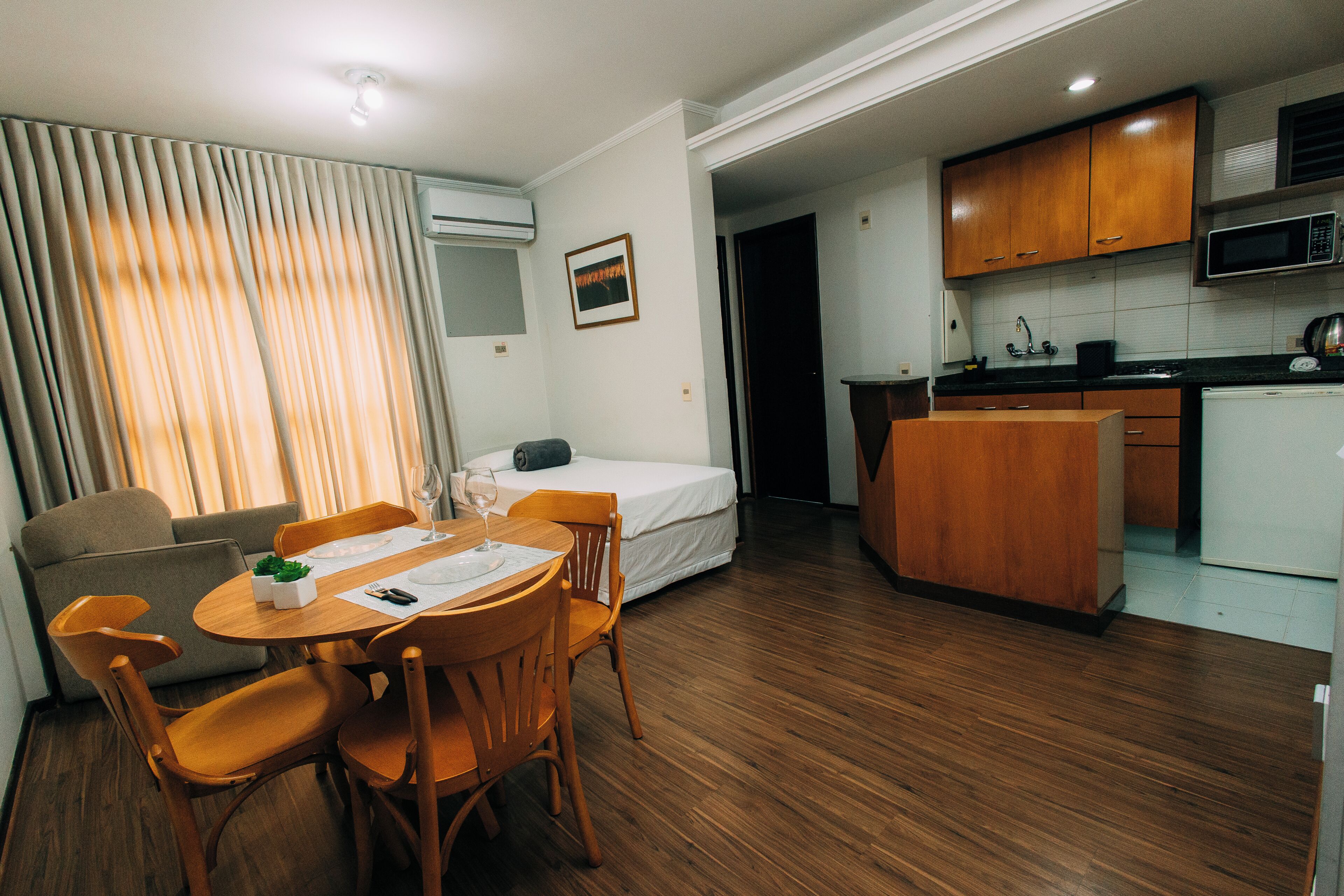 A compact hotel room with a dining area, kitchenette, and a bed.
