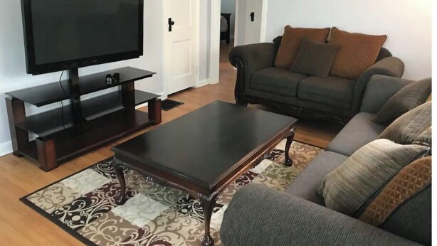 A living room with a flat-screen TV on a stand, a dark coffee table, a patterned rug, and a grey sofa with cushions. - Cheerful 2 bedroom home with parking on premises (Indianapolis)