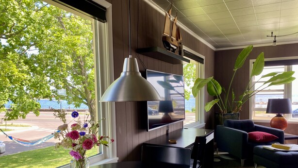 A modern living room with a large window, a dining table, a TV, and a sailboat decoration. - Avalon Guesthouse : Eastside Suite (Grand Marais)
