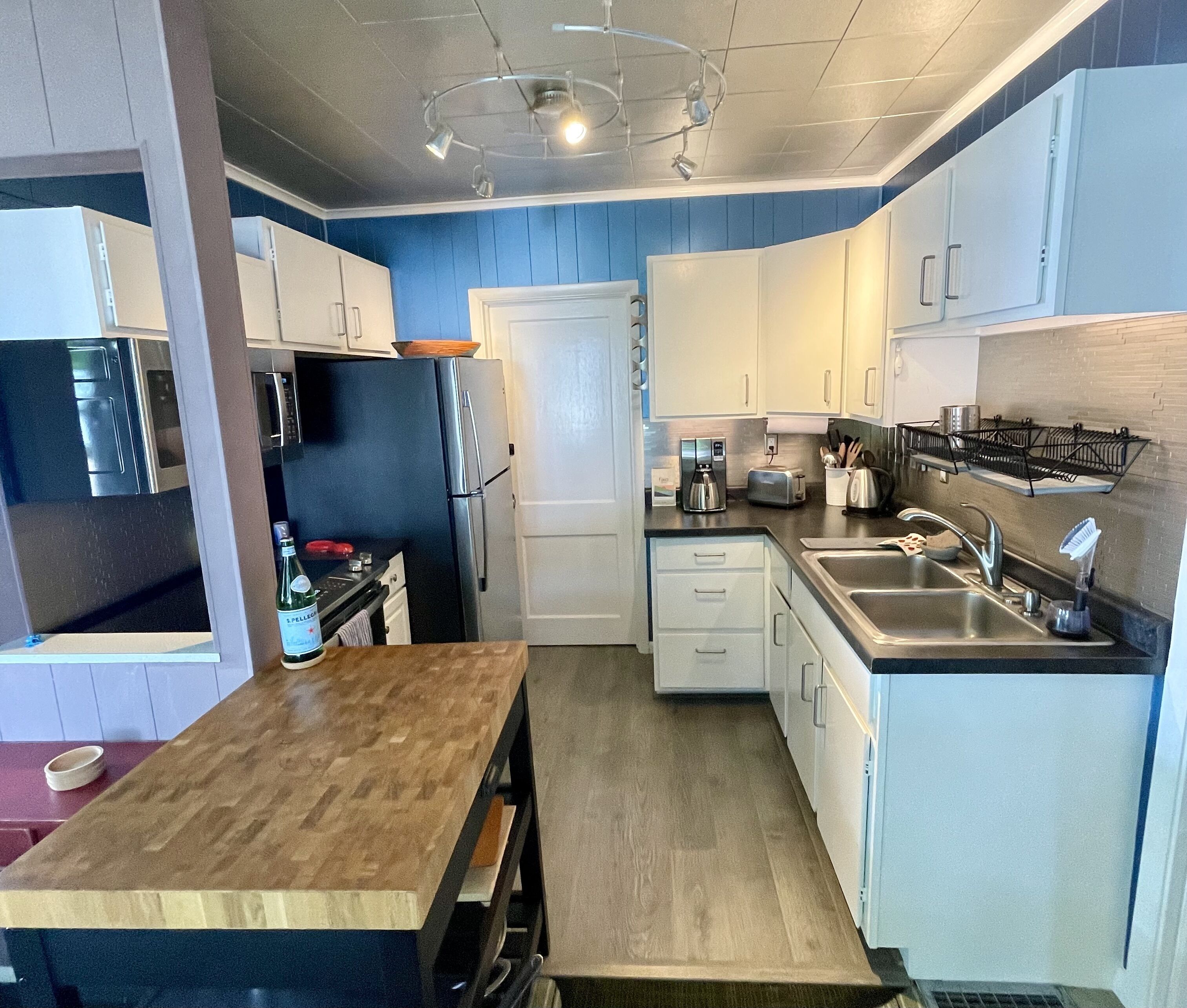 A modern kitchen with white cabinets, a wooden countertop, and stainless steel appliances.