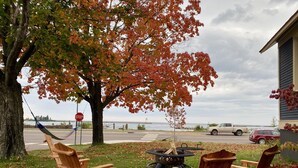 A wooden deck with Adirondack chairs, a fire pit, and a stop sign in the background. - Avalon Guesthouse : Eastside Suite (Grand Marais)
