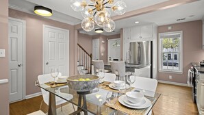 A modern kitchen with stainless steel appliances, a dining area with a glass table, and a staircase leading to another level. - Beautiful 3-Bdrm Home <> Park 2 Cars <> King Bed (Alexandria)
