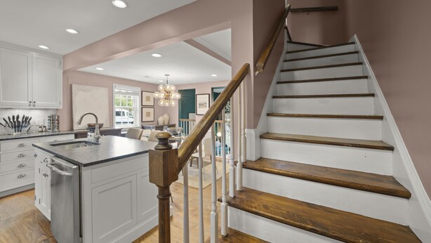 A modern kitchen with white cabinets, a central island, and a wooden staircase. - Beautiful 3-Bdrm Home <> Park 2 Cars <> King Bed (Alexandria)
