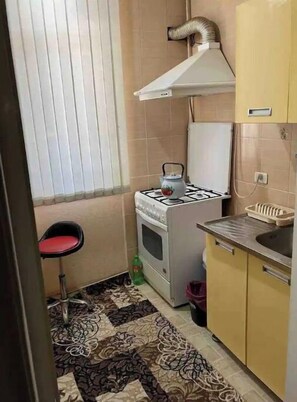 A compact kitchen with a gas stove, a small oven, a sink, and a chair.