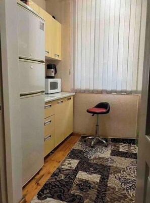 A small kitchen with a microwave, a refrigerator, and a chair.
