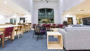 Un hall d’entrée spacieux avec un plafond haut, un espace de détente central agrémenté de tables et de chaises, une grande fenêtre et un design de plafond moderne.