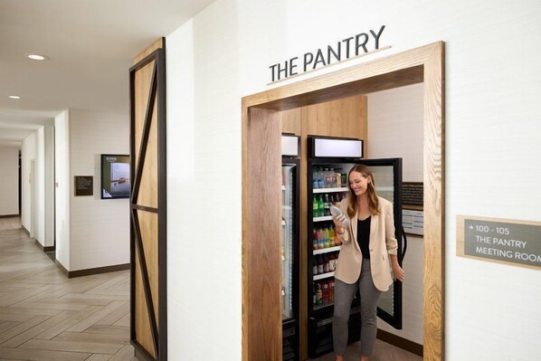 Een gang met een bordje met de tekst 'THE PANTRY' en een koelkast vol drankjes.